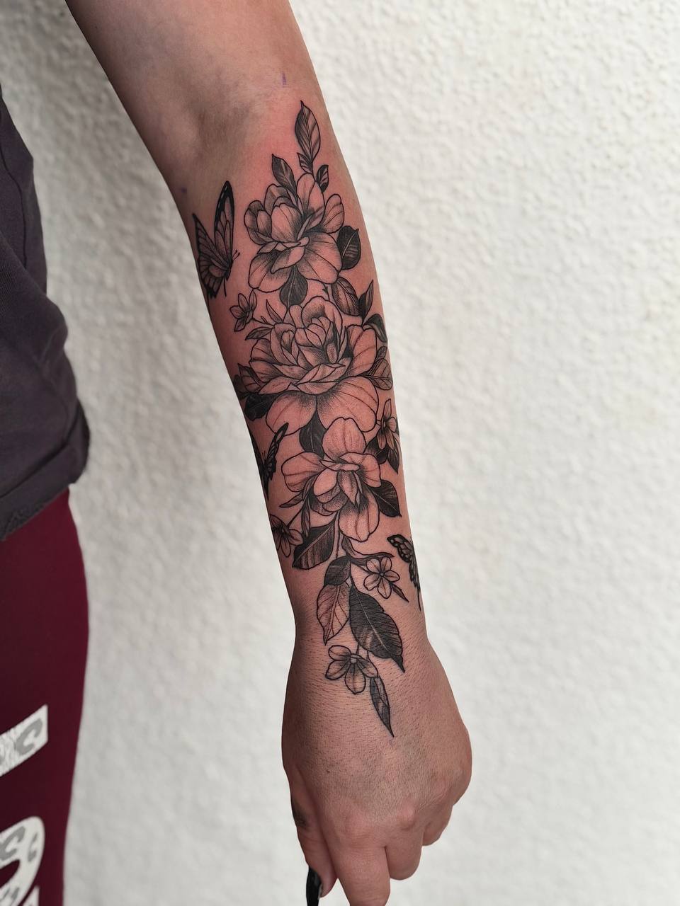 Florales Tattoo mit Blüten und Schmetterlingen am Unterarm